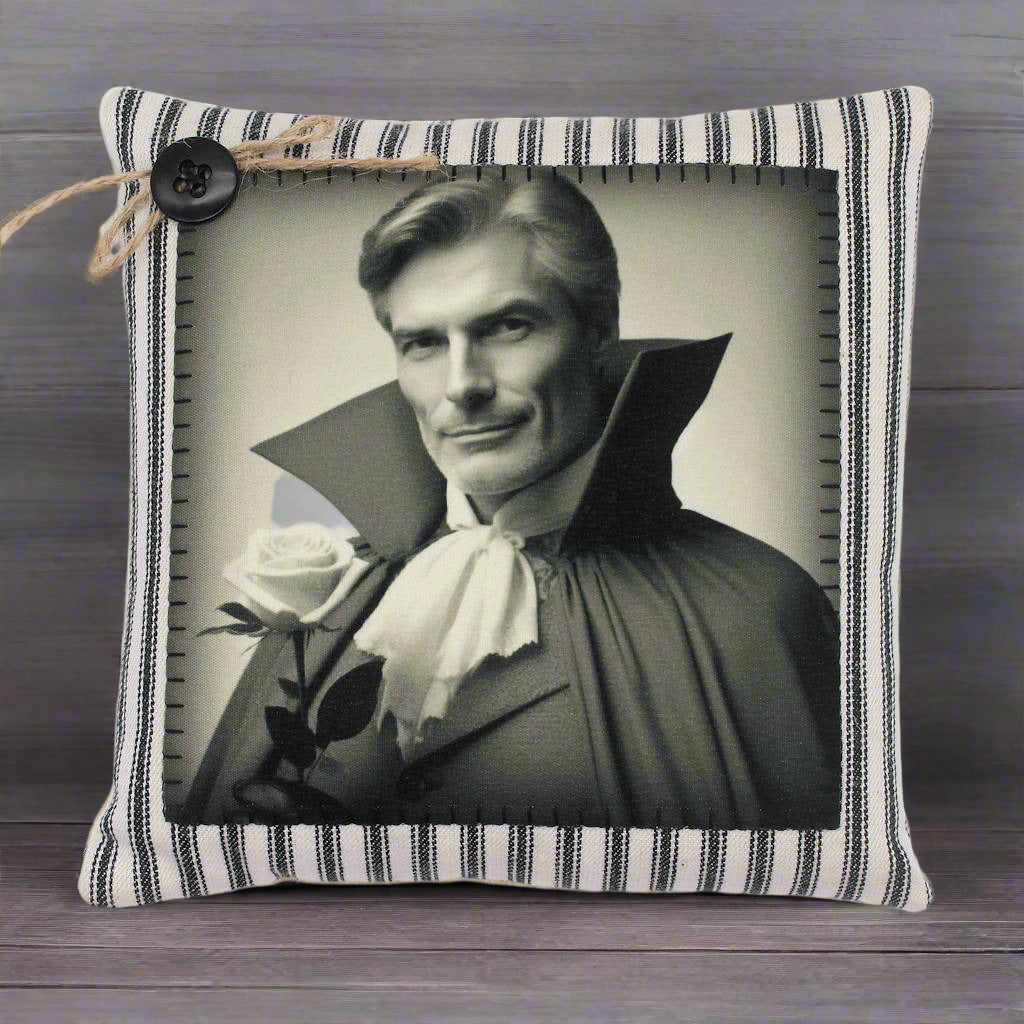 Decorative pillow with a black and white portrait of a handsome vampire in a cape and a rose, on a striped fabric background.