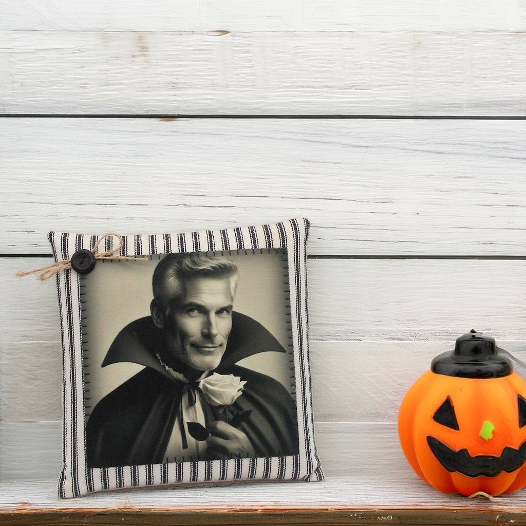 Decorative pillow with a portrait of a handsome vampire in a cape and a small pumpkin on a wooden surface.