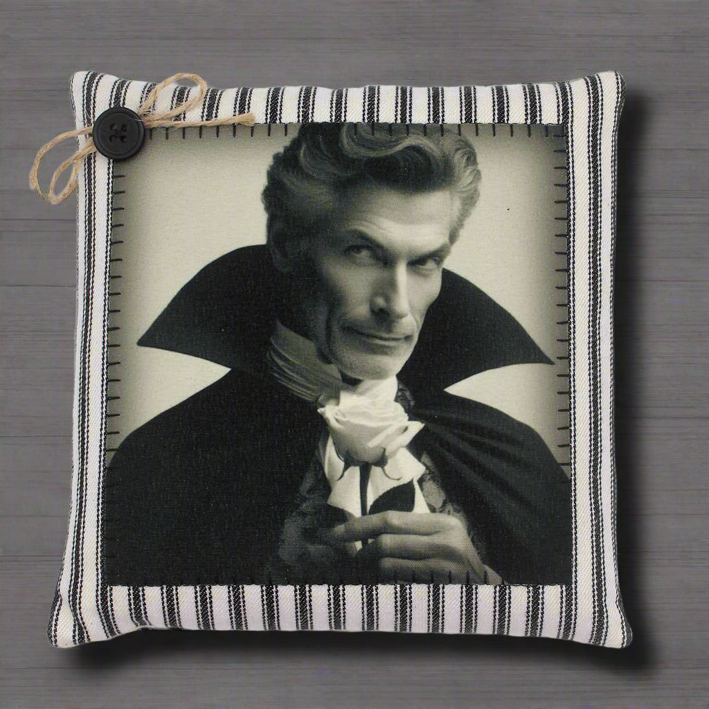 Decorative pillow with a black and white portrait of a handsome vampire in a cape holding a rose, framed by a striped border.