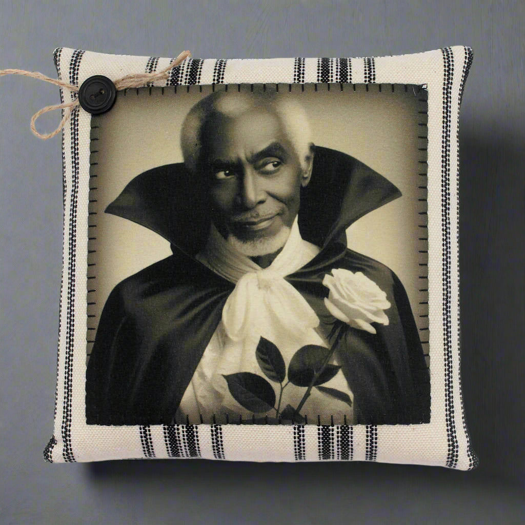 Pillow with a vintage-style print of a handsome vampire in a dark robe holding a white rose on a striped background.