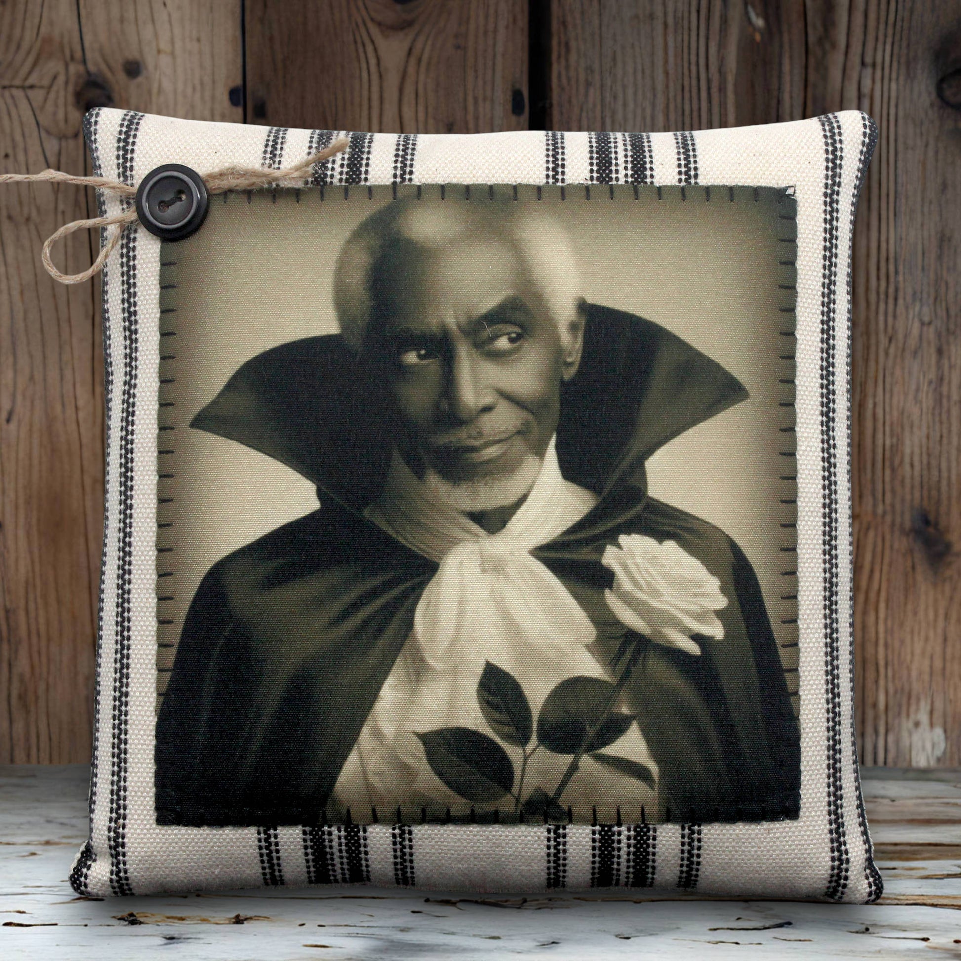 Pillow with a vintage-style print of a handsome vampire in a dark robe holding a white rose on a striped background.