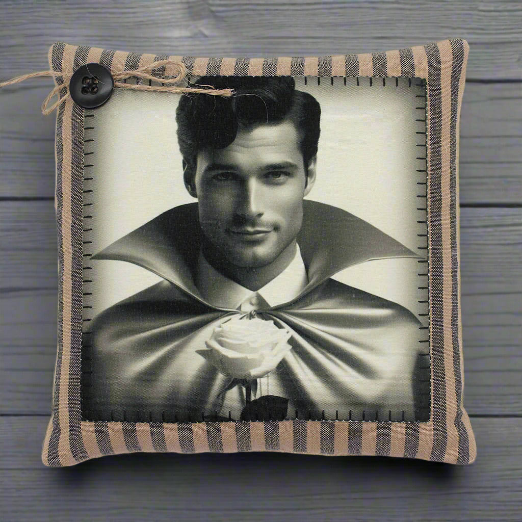 Pillow with a black and white portrait of a handsome young vampire in a cape holding a rose, framed by striped fabric.
