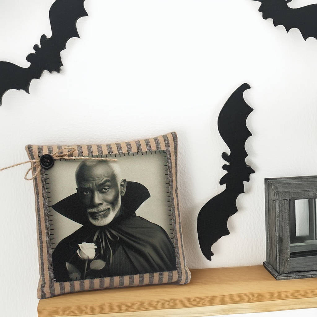 Decorative pillow with a vampire holding a rose on a shelf with bat-shaped decorations.