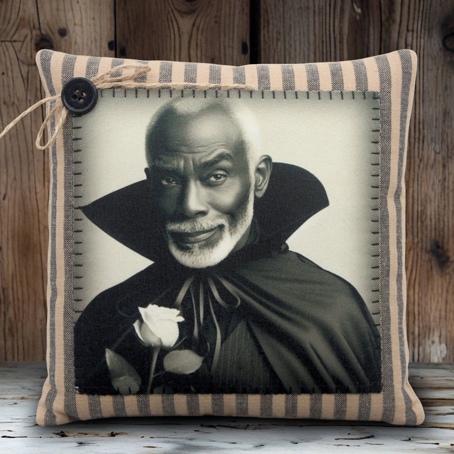 Pillow with a black and white portrait of a handsome vampire in a cape holding a rose, framed by striped fabric.
