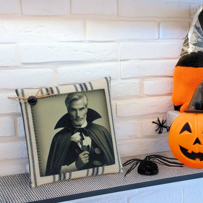 Decorative pillow with a handsome vampire in a cape and Halloween-themed pumpkins and spider on a white brick wall background.