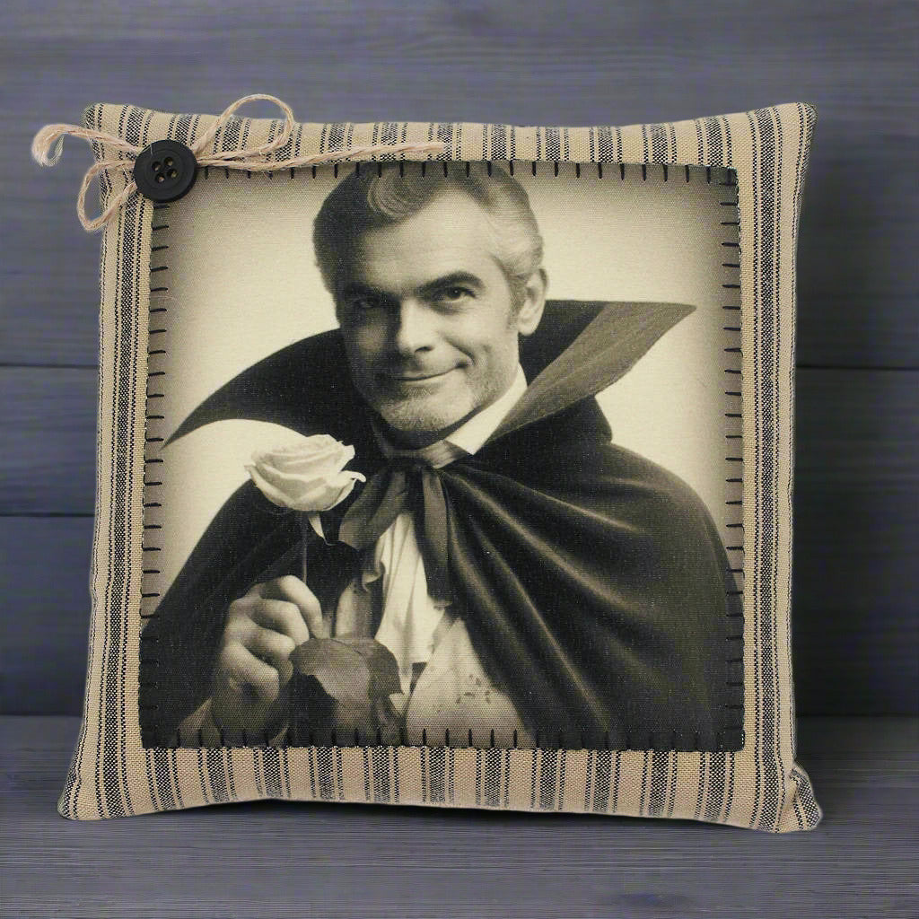Pillow with a vintage-style print of a handsome vampire in a cape holding a rose, framed by striped fabric.