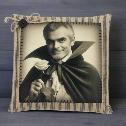 Pillow with a vintage-style print of a handsome vampire in a cape holding a rose, framed by striped fabric.