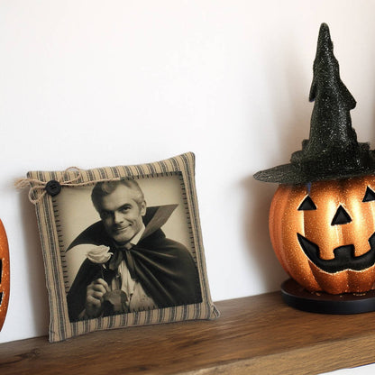 Decorative pillow with a portrait of a handsome vampire in a cape and a Halloween pumpkin on a shelf.
