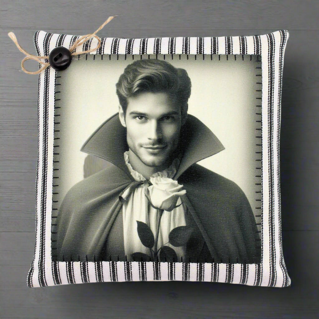 Decorative pillow with a black and white portrait of a handsome young vampire in a cape holding a rose, on a striped background.