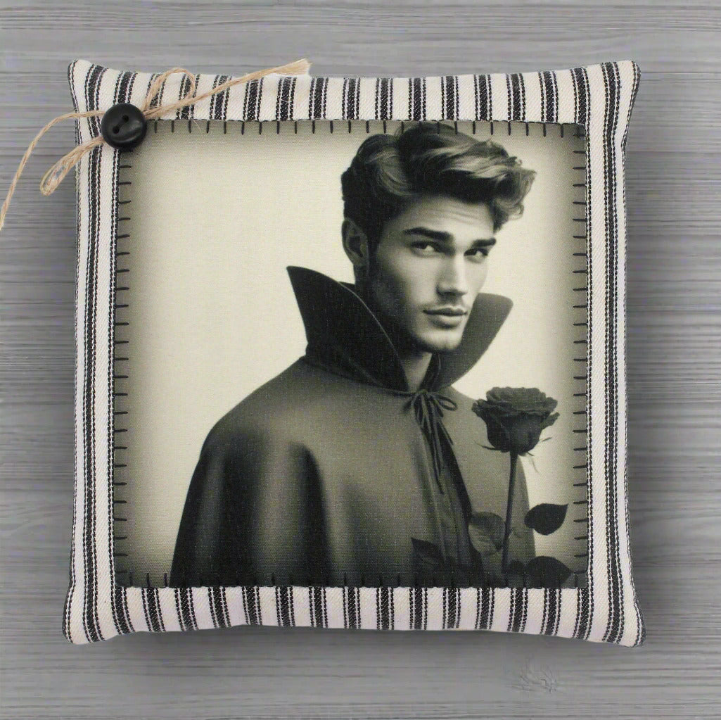 Decorative pillow with a black and white photo of a handsome young vampire in a cape holding a rose, on a striped fabric background.