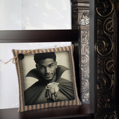 Decorative pillow with a black and white portrait of a handsome young vampire holding a rose, placed on a wooden surface.
