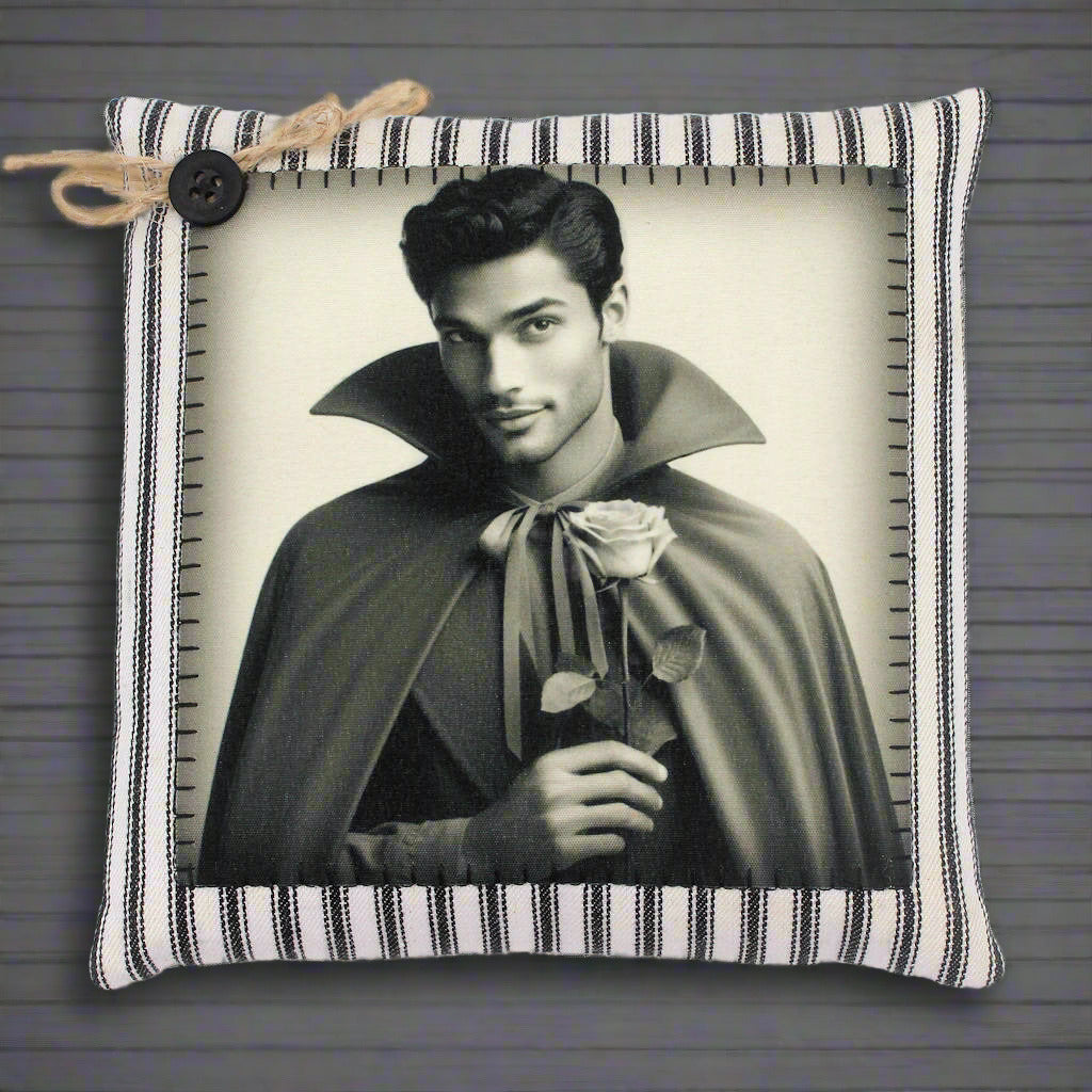 Decorative pillow with a black and white print of a handsome young vampire in a cape holding a rose, on a striped fabric background.