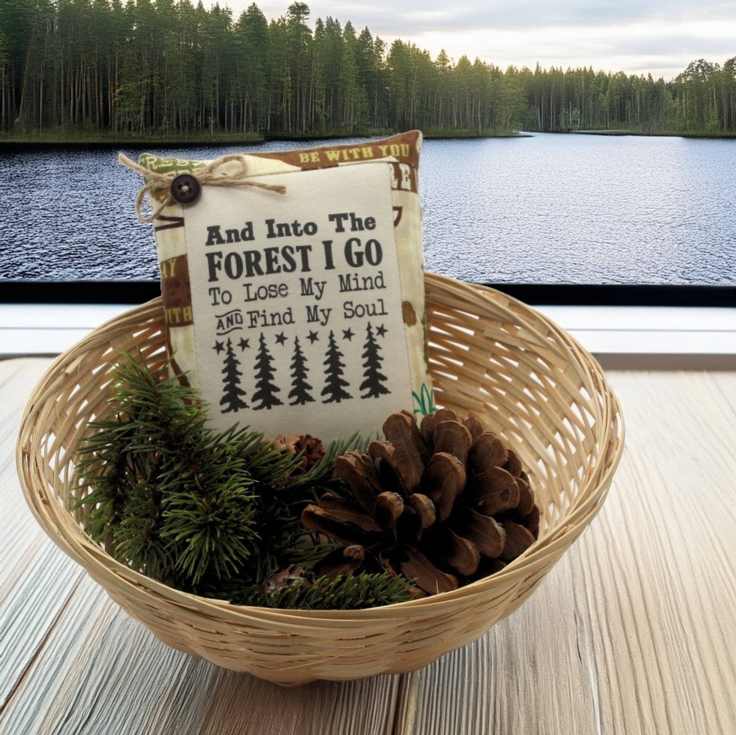 Decorative basket with a pillow and pinecones by a lake with trees in the background