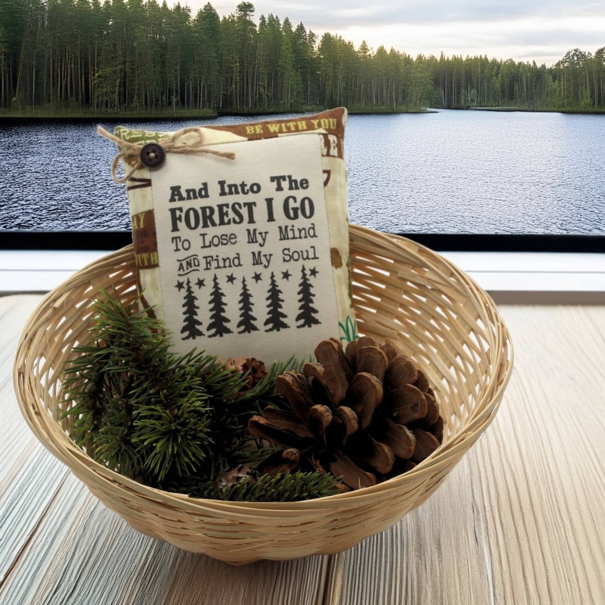 Decorative basket with a pillow and pinecones by a lake with trees in the background