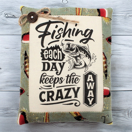 Decorative pillow tuck with fishing-themed text and graphics on a wooden surface
