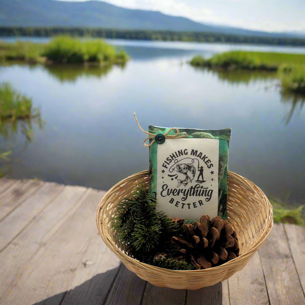 Decorative pillow with 'Fishing Makes Everything Better' text in a woven basket by a lake.
