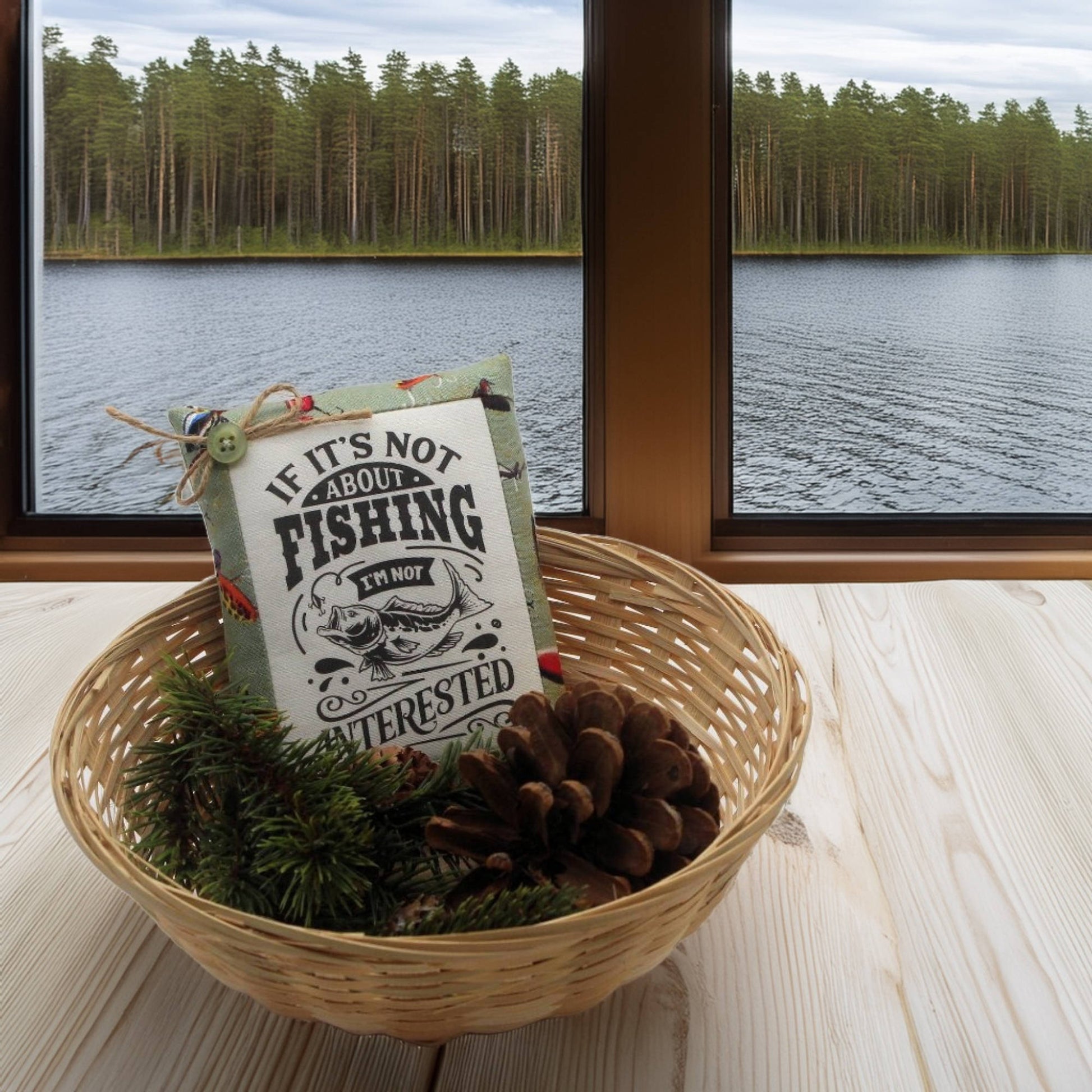 Decorative basket with a fishing-themed pillow and pinecones, set against a scenic lake view.
