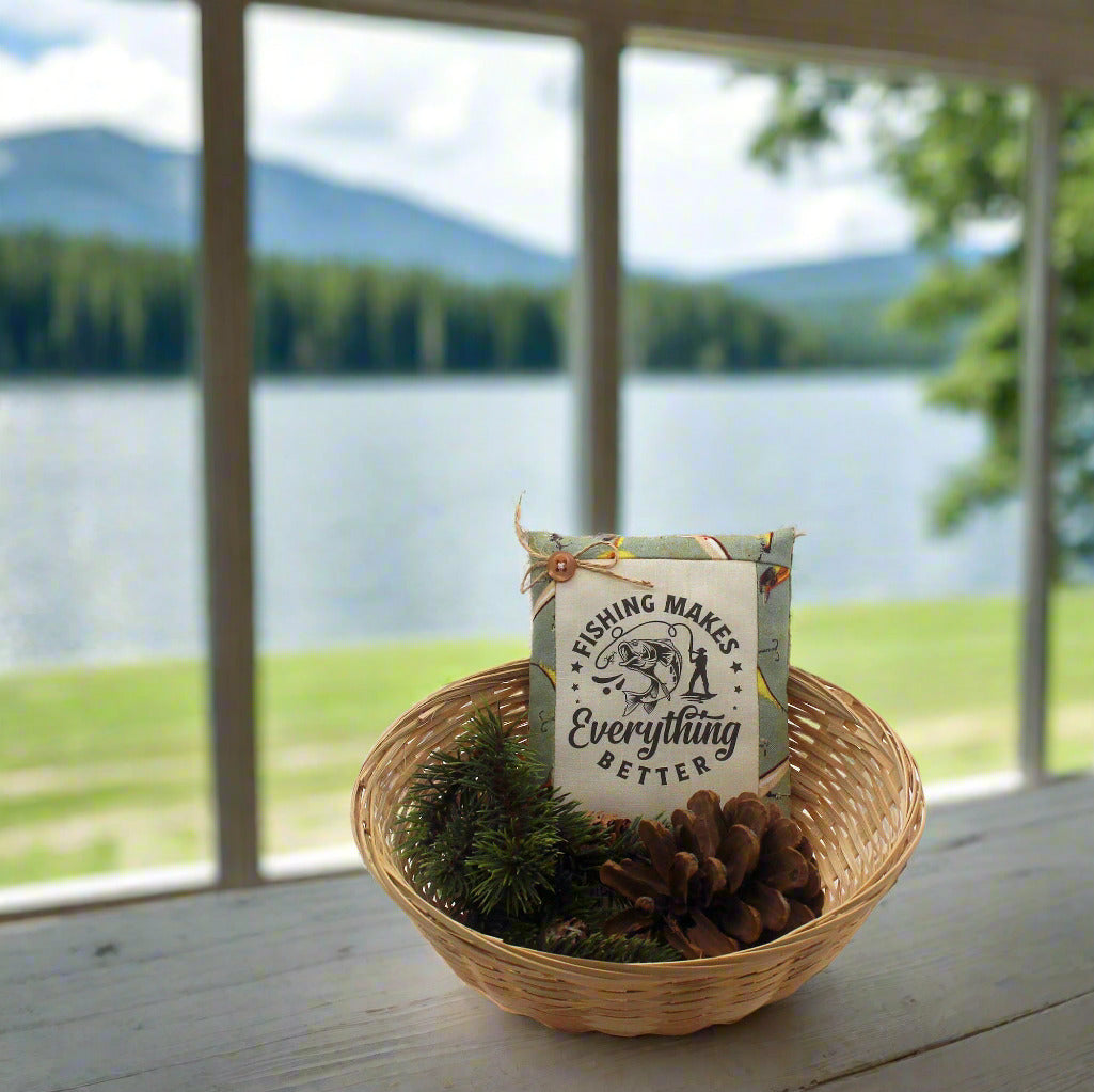 Decorative basket with a 'Fishing Makes Everything Better' sign in front of a window with a view of a lake and mountains.