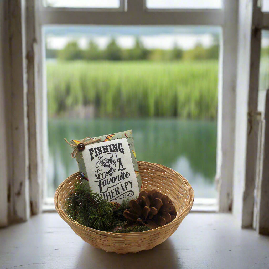 Decorative basket with a sign and pinecones in front of a window with a view of water and greenery.