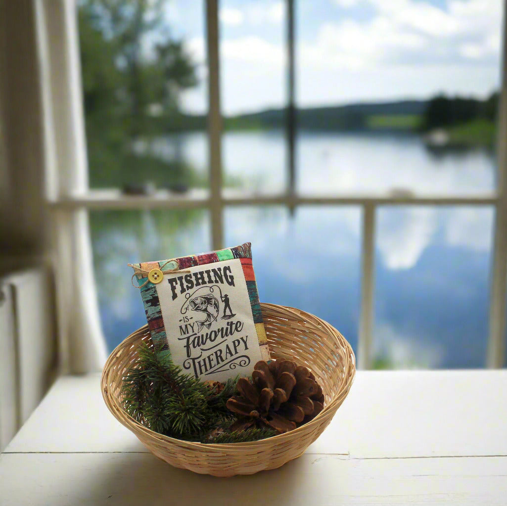 Decorative basket with a fishing-themed pillow and pinecones on a windowsill with a lake view.