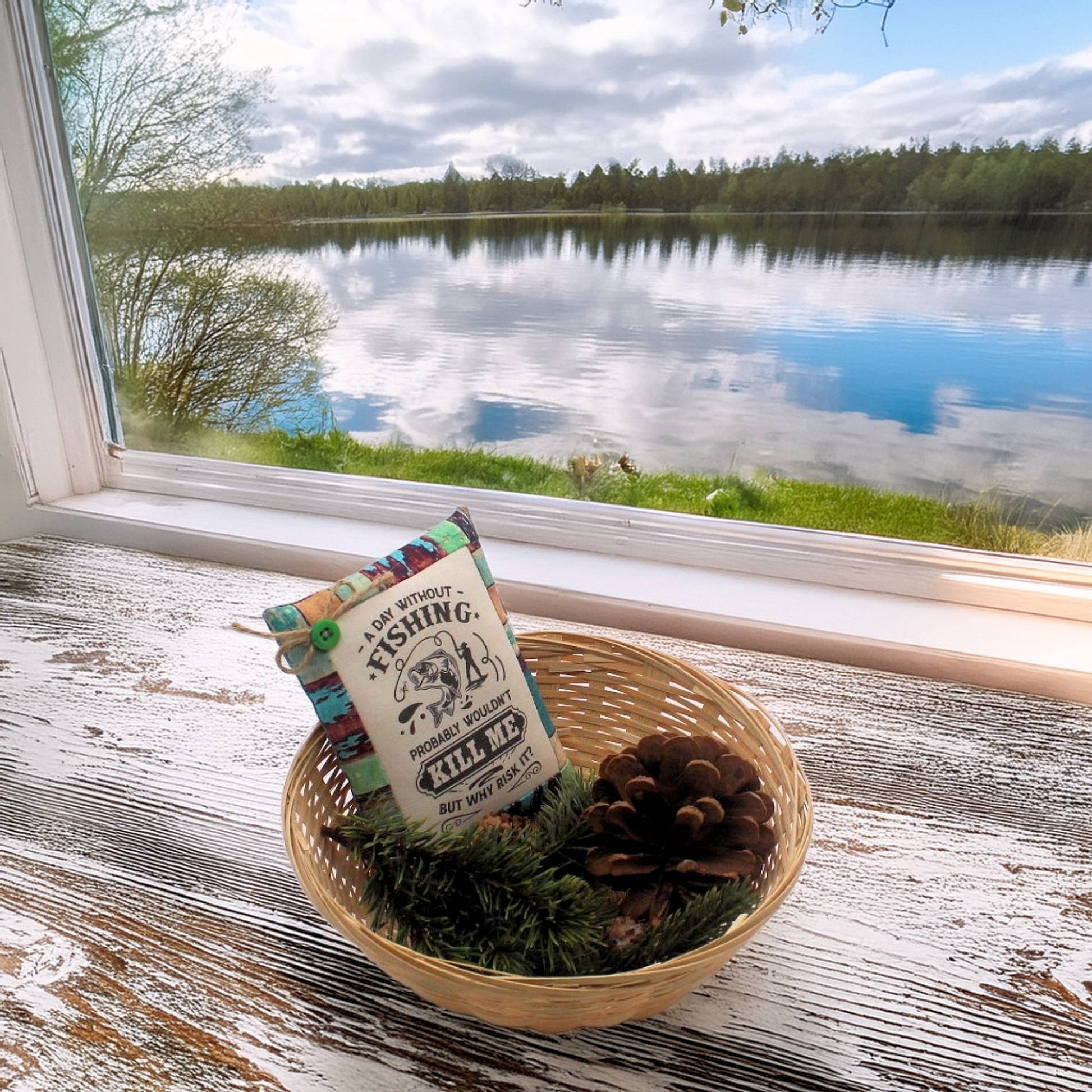 Decorative pillow with fishing design in a woven basket by a window with a view of a lake.
