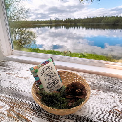 Decorative pillow with fishing design in a woven basket by a window with a view of a lake.