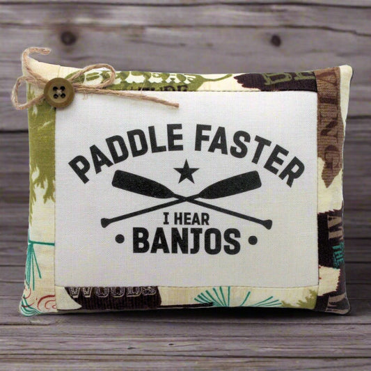 Pillow bowl filler with 'Paddle Faster, I Hear Banjos' text and oar design on a wooden surface