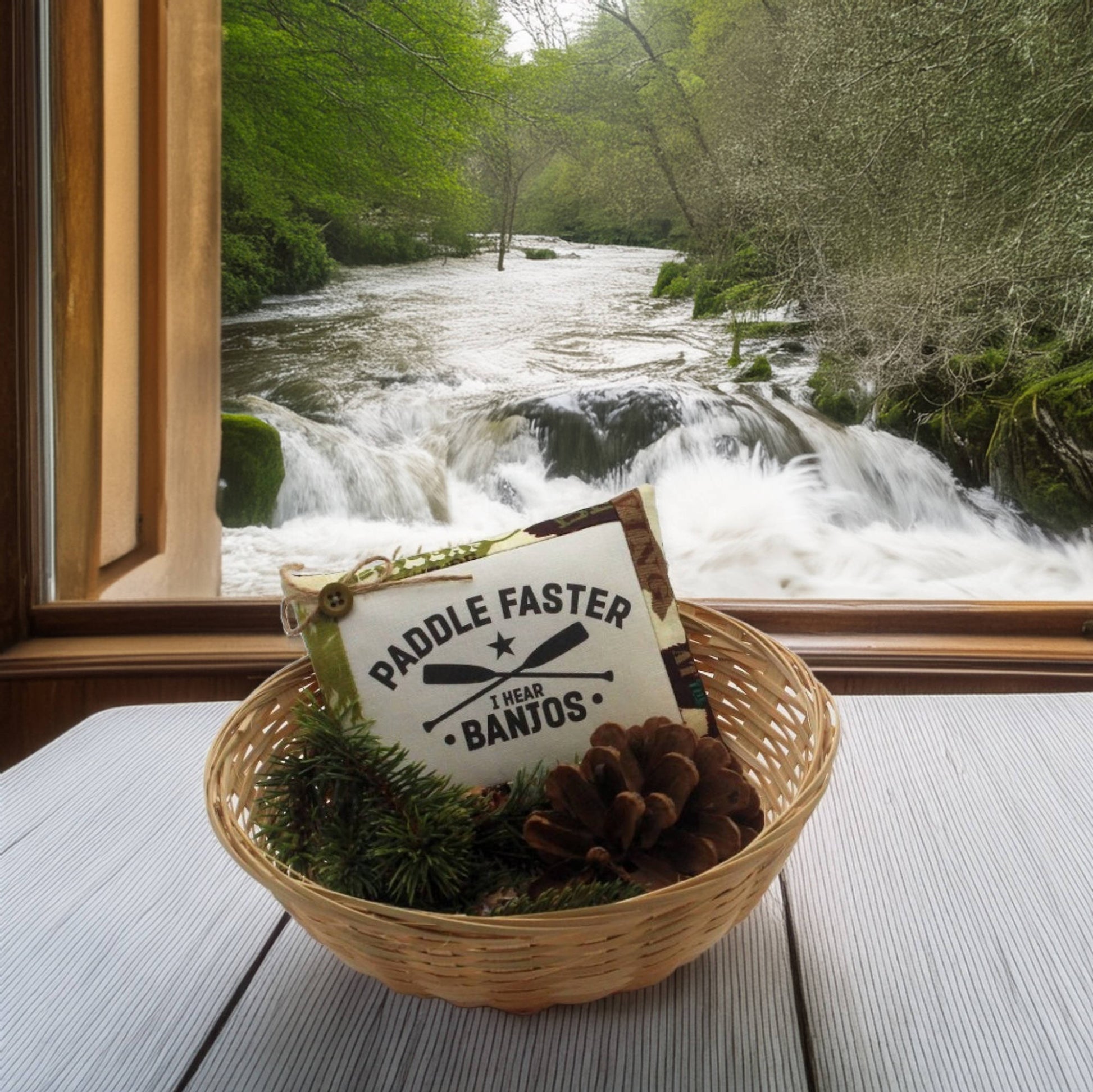 Decorative basket with a 'Paddle Faster Wear Banjos' sign in front of a window with a view of a river.