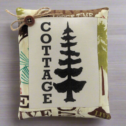 Fabric pillow tuck with 'Cottage' and tree design on a wooden surface