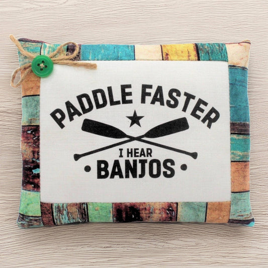 Decorative pillow bowl filler with 'Paddle Faster, I Hear Banjos' text and oar design on a wooden background.