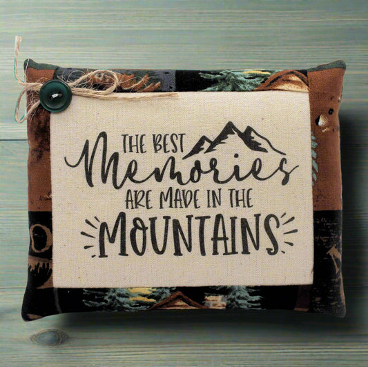 Pillow tuck with 'The best memories are made in the mountains' text and mountain graphic on a natural background.