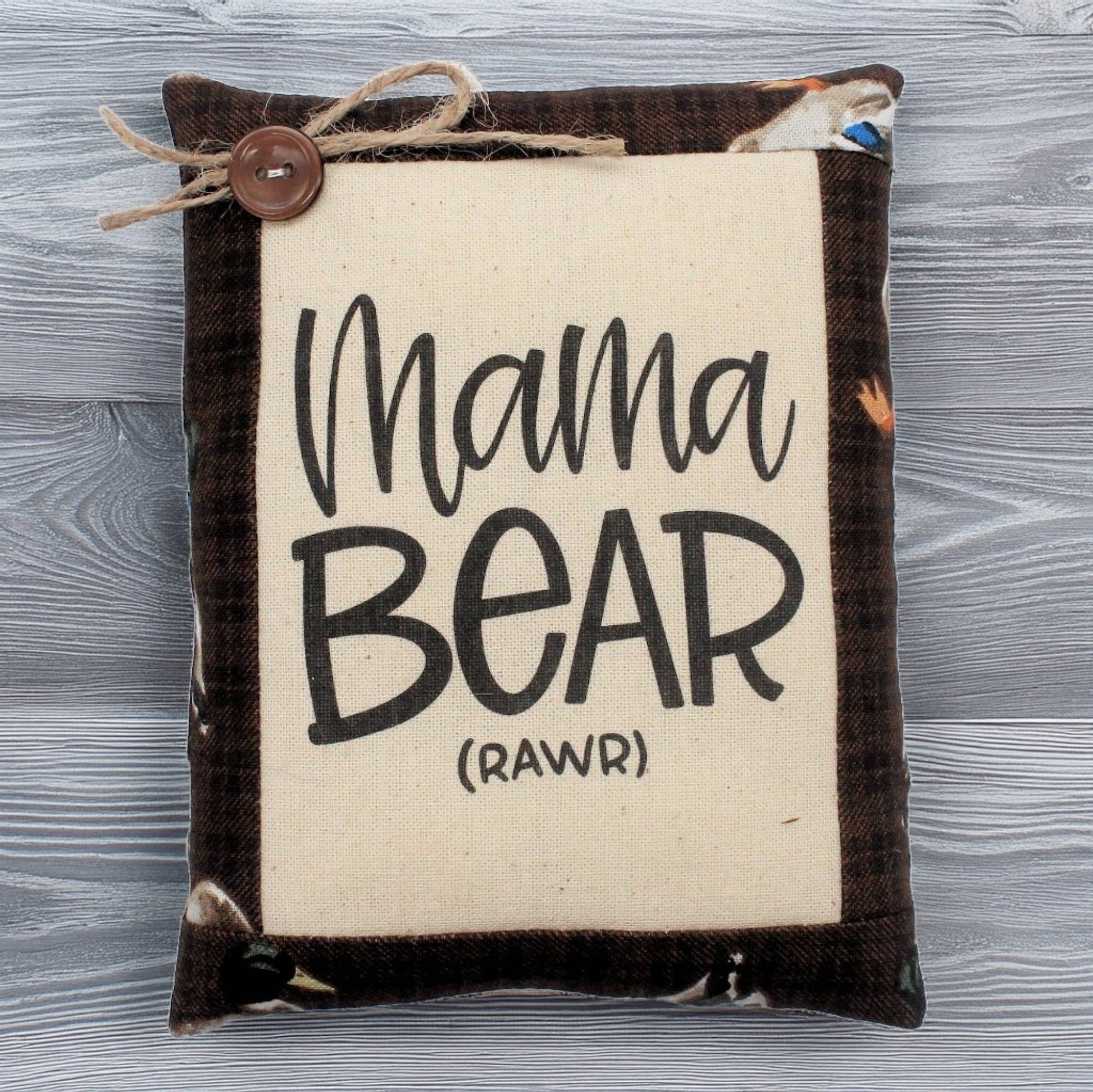 Small pillow with 'Mama Bear (Rawr)' text on a wooden surface