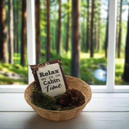 Decorative basket with a sign and pinecones in front of a window with a forest view
