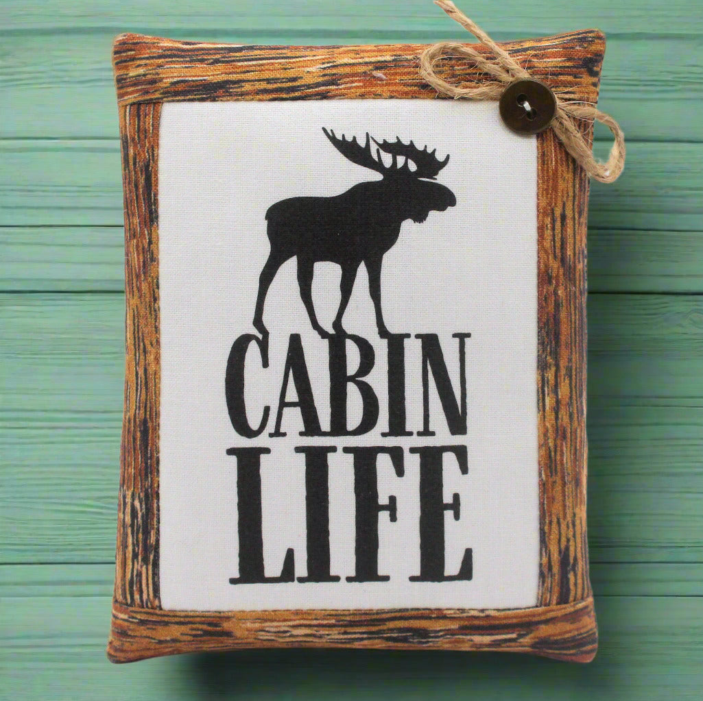Decorative mini pillow sign with moose silhouette and 'Cabin Life' text on a wooden frame against a green background.