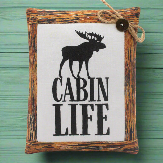 Decorative mini pillow sign with moose silhouette and 'Cabin Life' text on a wooden frame against a green background.