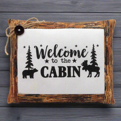 Decorative mini pillow bowl filler with 'Welcome to the Cabin' text and nature-themed illustrations on a wooden frame.