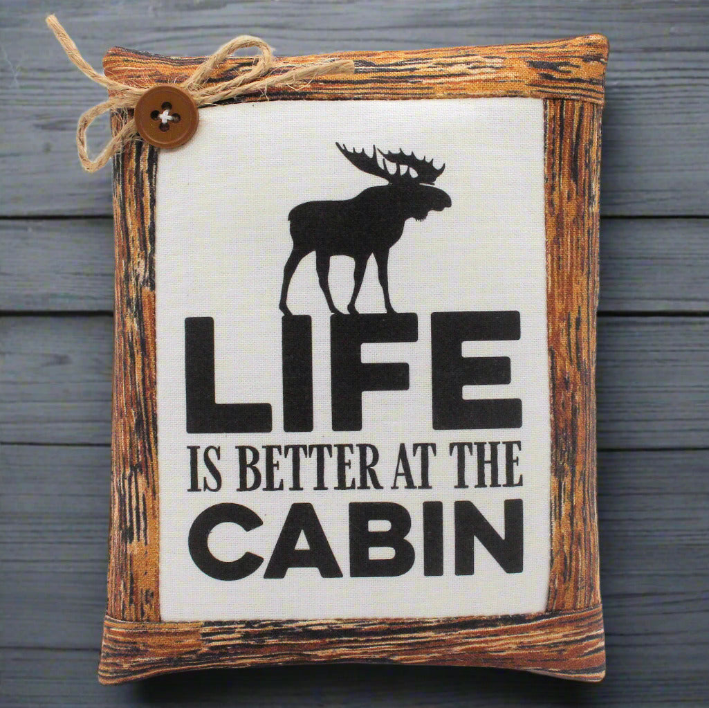 Decorative mini pillow sign with a moose silhouette and 'Life is Better at the Cabin' text on a wooden frame.