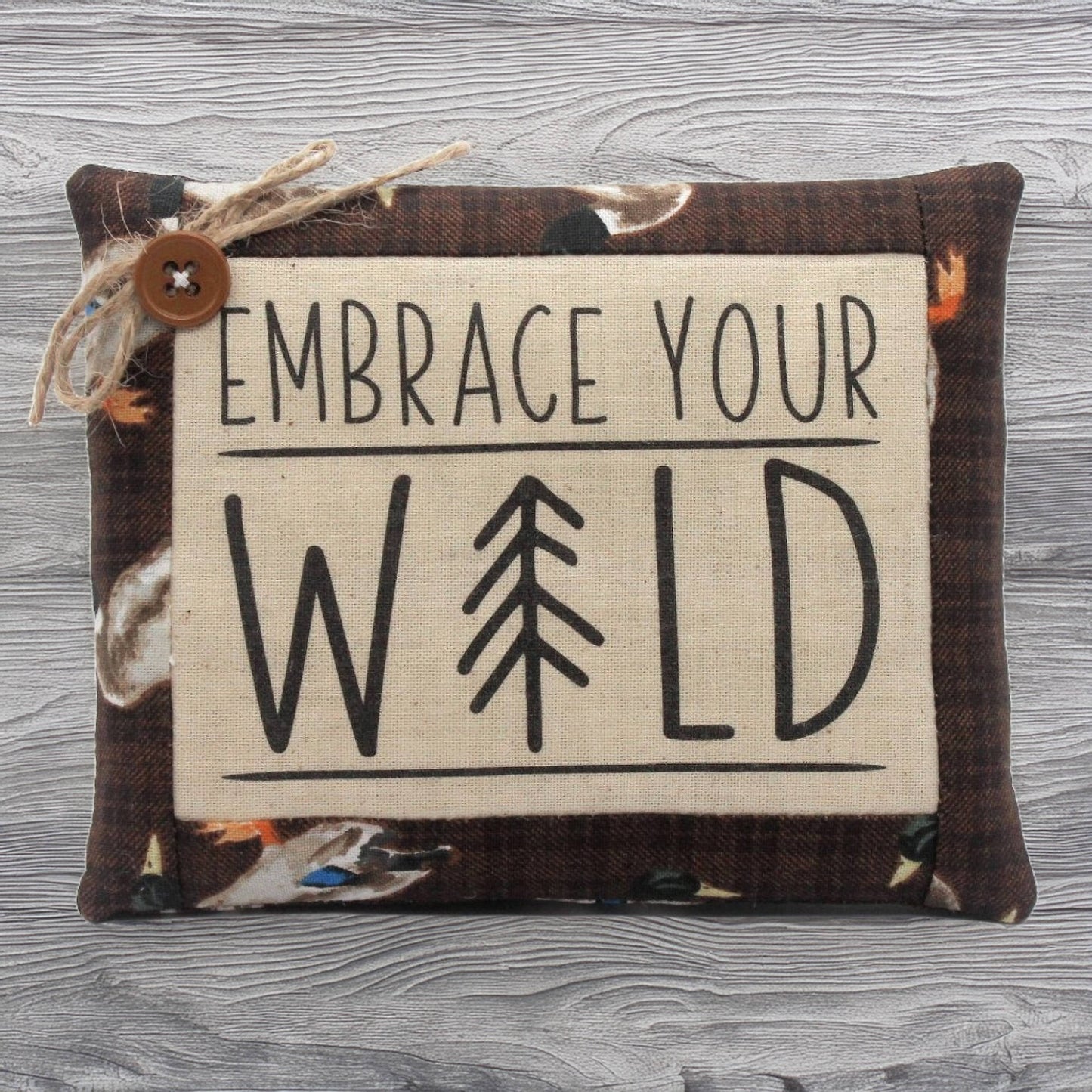 Decorative pillow tuck with 'Embrace Your Wild' text and tree symbol on a wooden surface