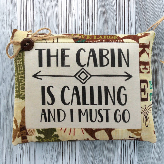 Pillow tuck with text 'The cabin is calling and I must go' on a wooden surface