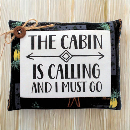 Decorative mini pillow with text 'The cabin is calling and I must go' on a wooden background