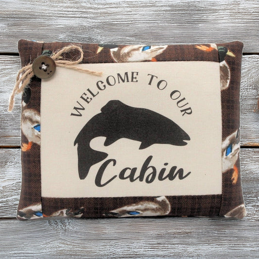 Decorative pillow tuck bowl filler with 'Welcome to our Cabin' text and fish silhouette on a wooden background