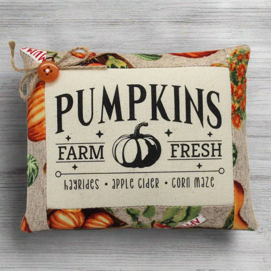 Decorative pillow with 'Pumpkins Farm Fresh' text and pumpkin illustrations on a wooden surface.