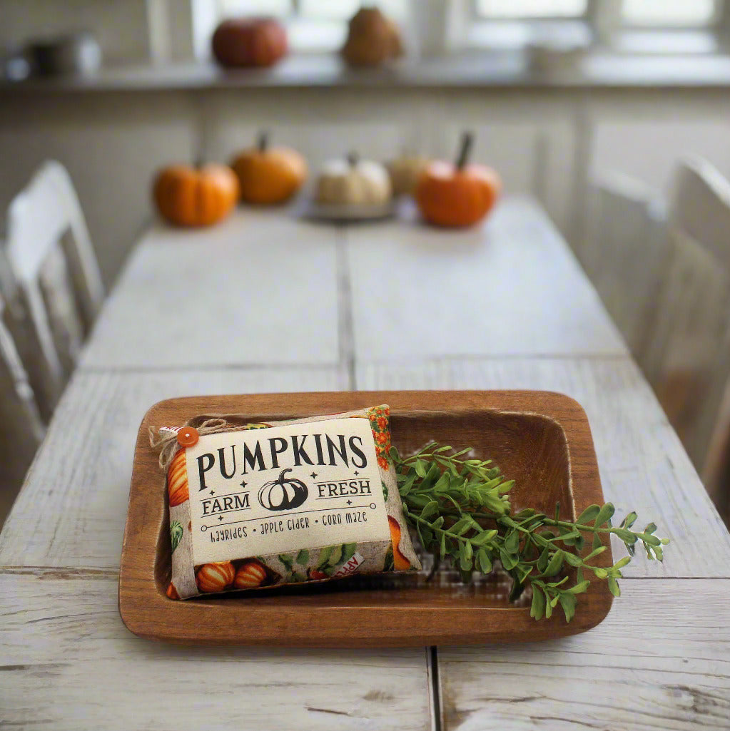 Wooden tray with a 'Pumpkins Farm Fresh' bag and greenery on a wooden table.