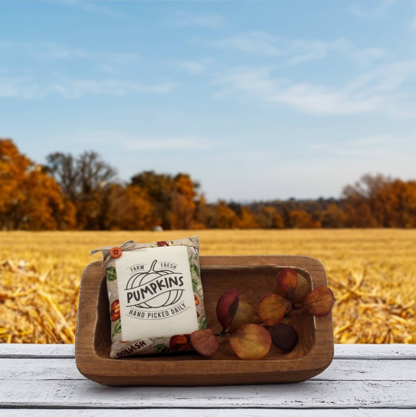 Wooden bowl with a 'Farm Fresh Pumpkins' pillow tuck against a field background