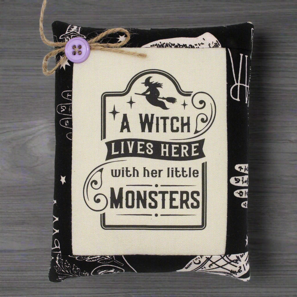 Decorative pillow with 'A Witch Lives Here with her little Monsters' text on a wooden surface