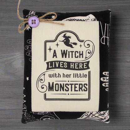 Decorative pillow with 'A Witch Lives Here with her little Monsters' text on a wooden surface