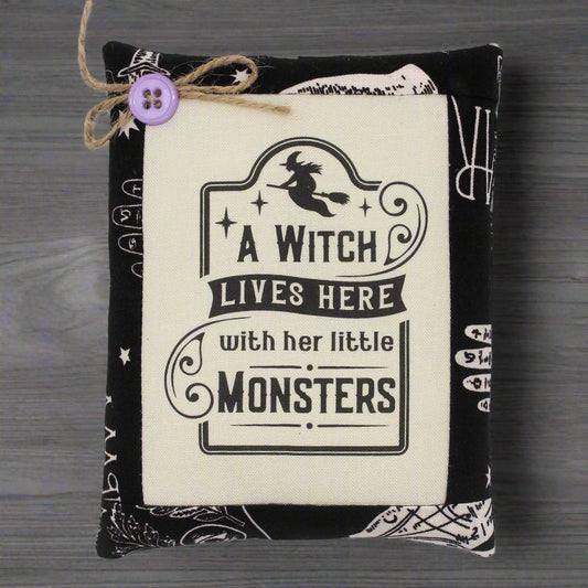 Decorative pillow with 'A Witch Lives Here with her little Monsters' text on a wooden surface