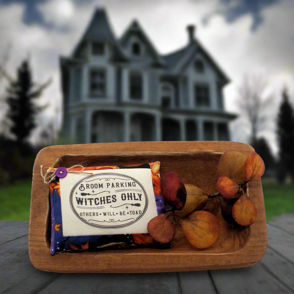 Wooden tray with Halloween-themed items including brooms and a sign in front of a spooky house.