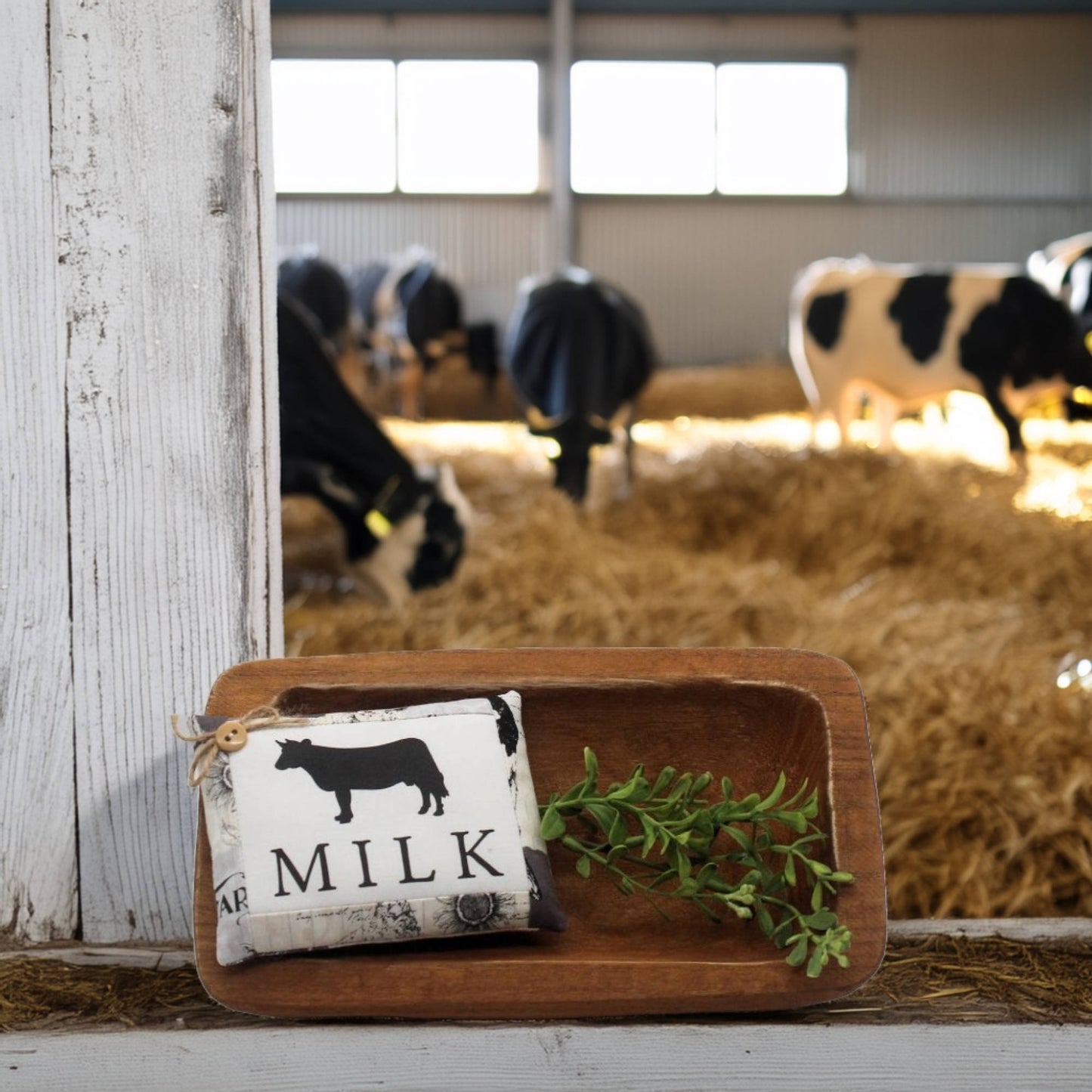 Wooden tray with a 'Milk' sign and cow illustration in a barn setting with cows in the background.