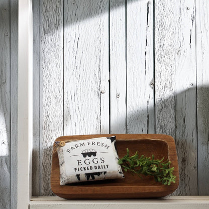 Wooden tray with a decorative pillow and greenery against a wooden wall.